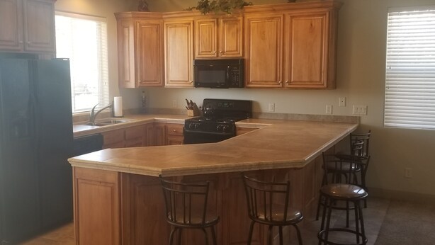 A kitchen with wooden cabinets, a black stove, a microwave, and a bar area with stools. - Las Palmas. Great place for a getaway (St. George)