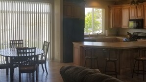 A kitchen with wooden cabinets, a central island with bar stools, a dining table with chairs, and a large window with blinds. - Las Palmas. Great place for a getaway (St. George)