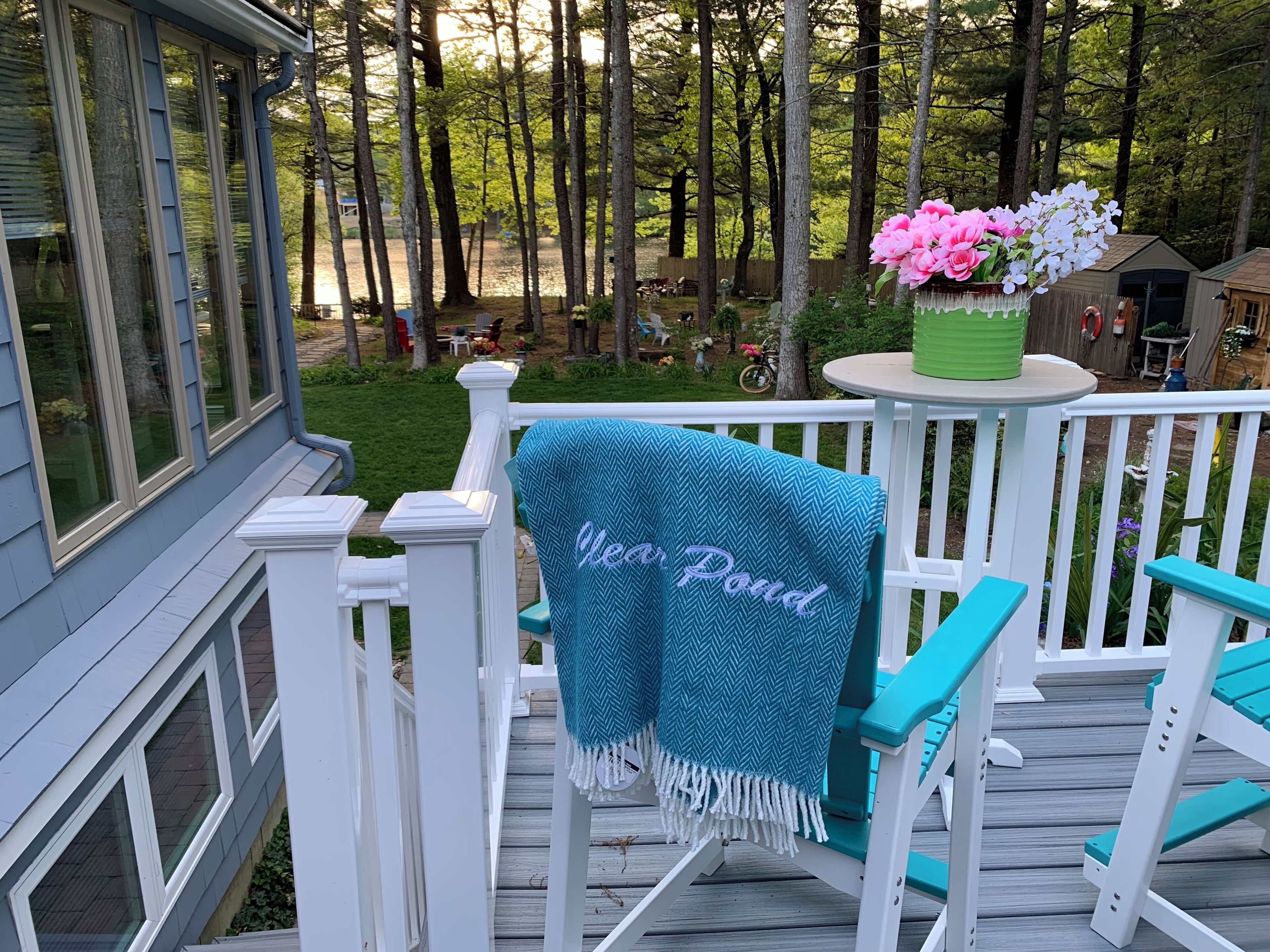 Une terrasse en bois avec un espace salon couvert, une petite table agrémentée d’une plante en pot et une vue sur une zone boisée.
