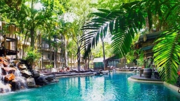 Una piscina con cascada, rodeada de exuberante vegetación y un edificio de diseño moderno.