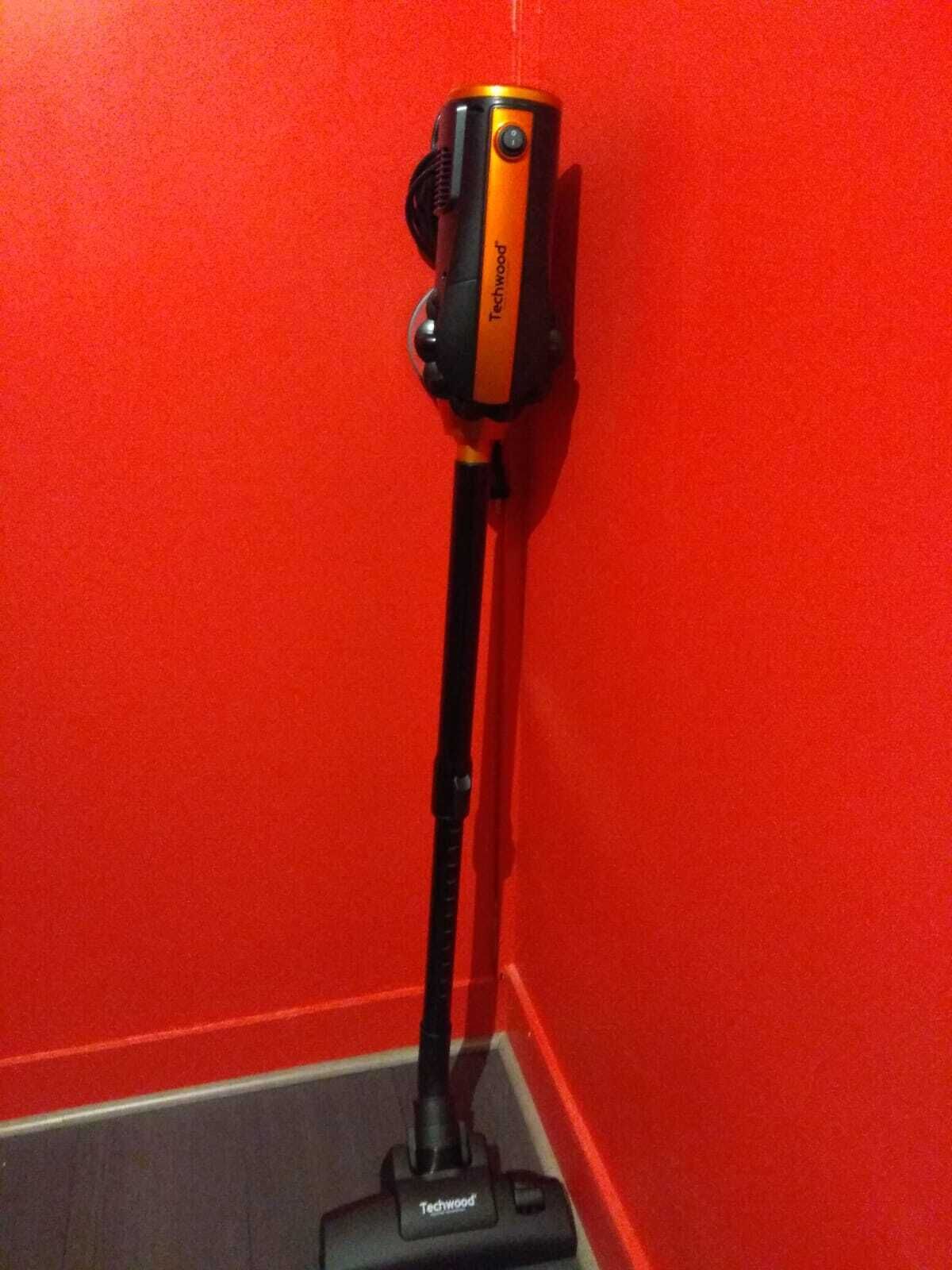 Aspiradora con una manguera larga frente a una pared roja.