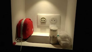 Una estantería pequeña y blanca con una bolsa roja, un dispensador de gel hidroalcohólico y una toma de corriente.