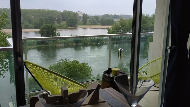 Un balcón con vista a un río, una hamaca y dos vasos de martini sobre una mesa de madera.