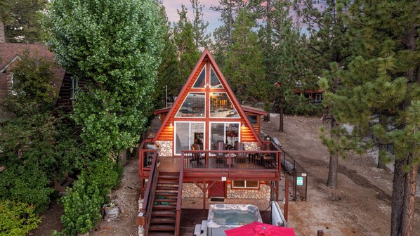 A cabin with a balcony, a hot tub, and a stone wall.