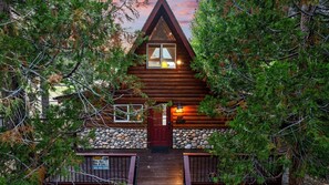 A log cabin with a stone foundation, a red door, and a small porch.