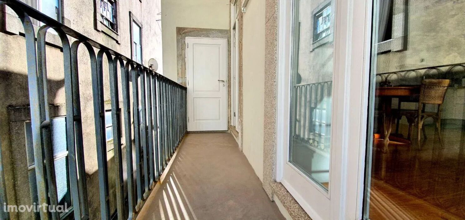 A narrow hallway with a metal railing, a white door at the end, and a window on the right side.