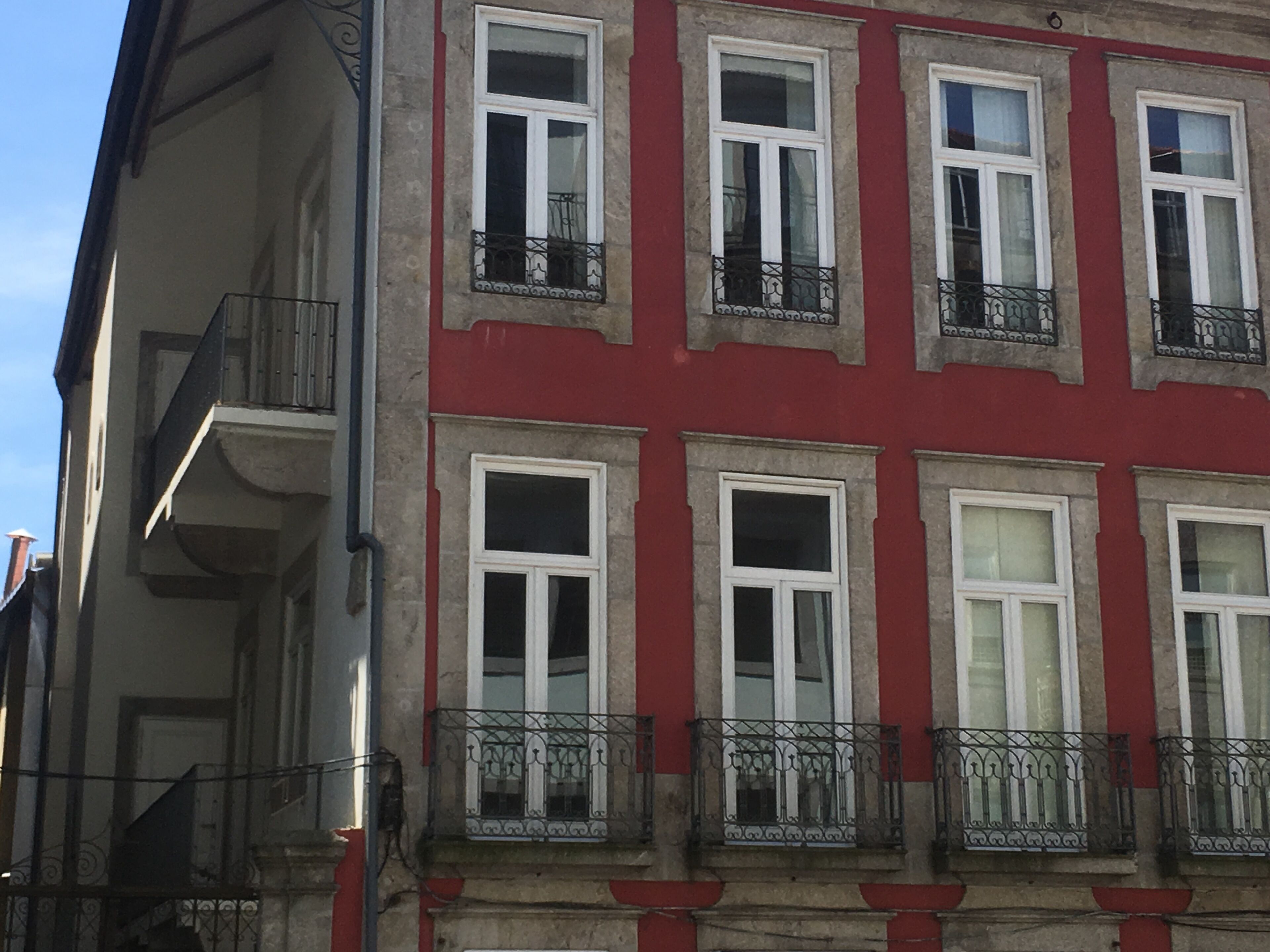 A multi-story building with red and white exterior walls, multiple windows with black wrought iron balconies, and a visible staircase on the left side.