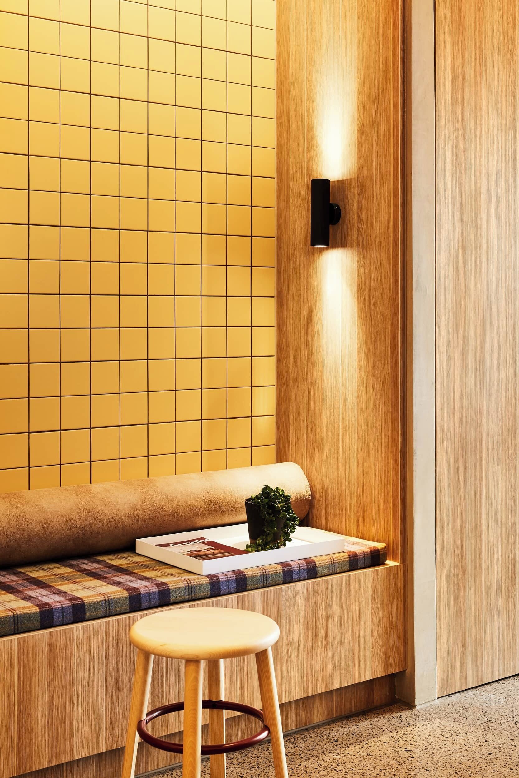 Een modern interieur met een houten bankje, een klein krukje en een muur met een rasterpatroon.