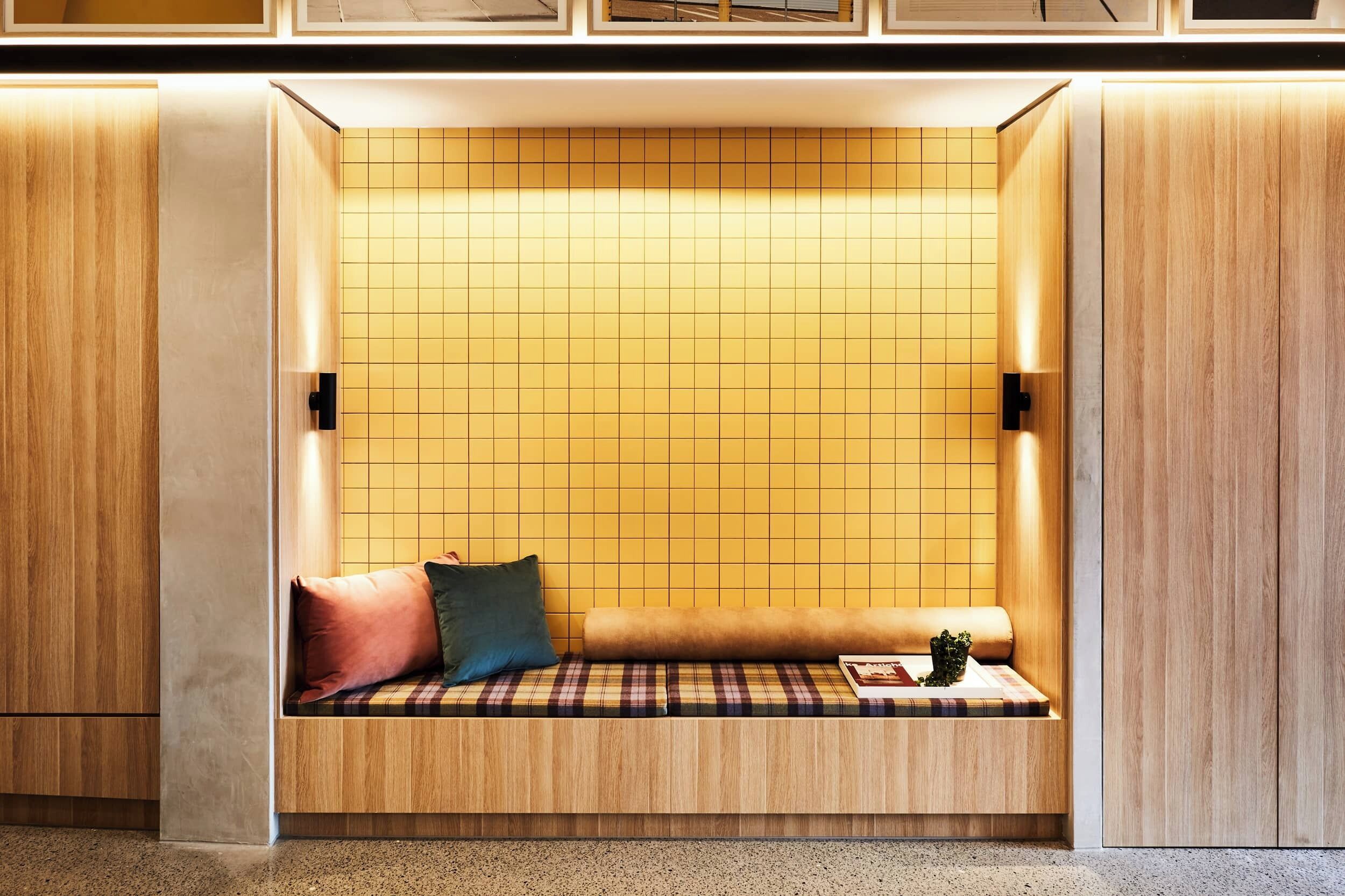 A cozy seating area with a checkered bench, a small table, and two wall-mounted lights.