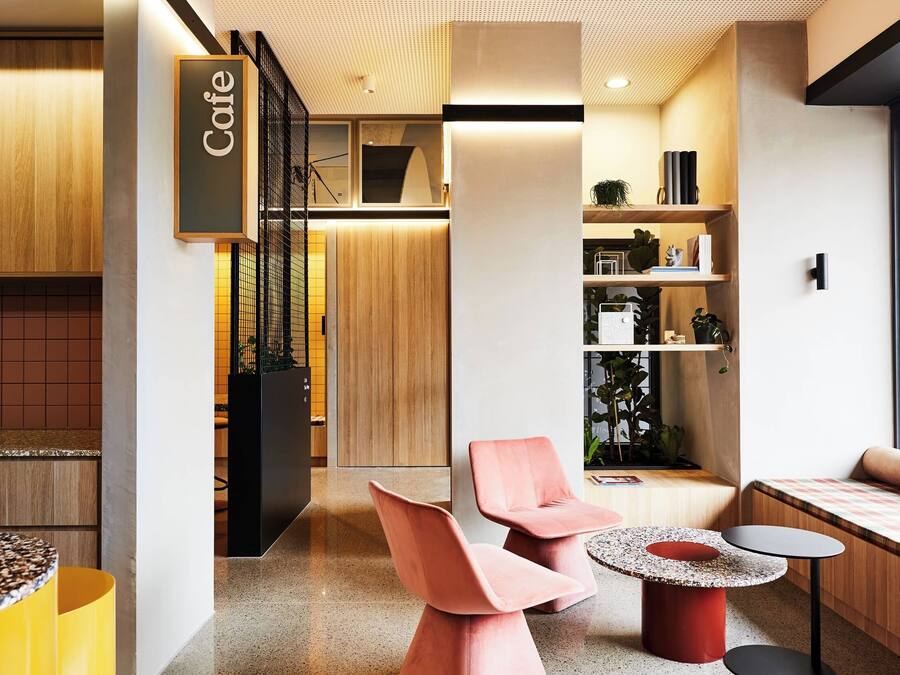 Un café moderno con interior de madera, una zona de estar con un banco y sillas, y un letrero que dice 'Cafe'.