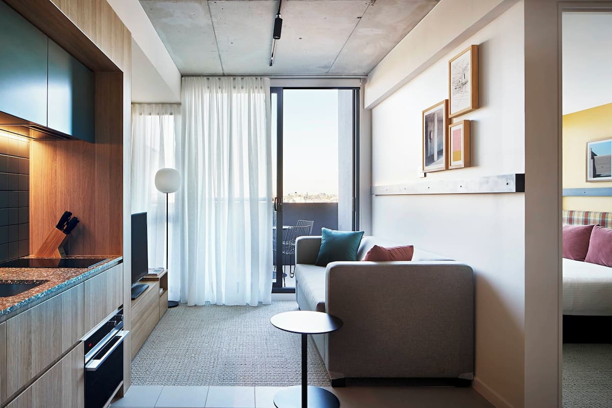 Una habitación de hotel moderna con kitchenette, un sofá, una mesita redonda y un balcón con vistas.