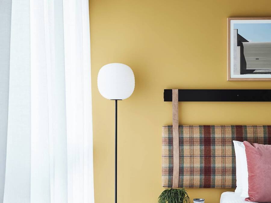 A bedroom with a bed, a bedside table with a lamp, a small plant, and a framed picture on the wall.