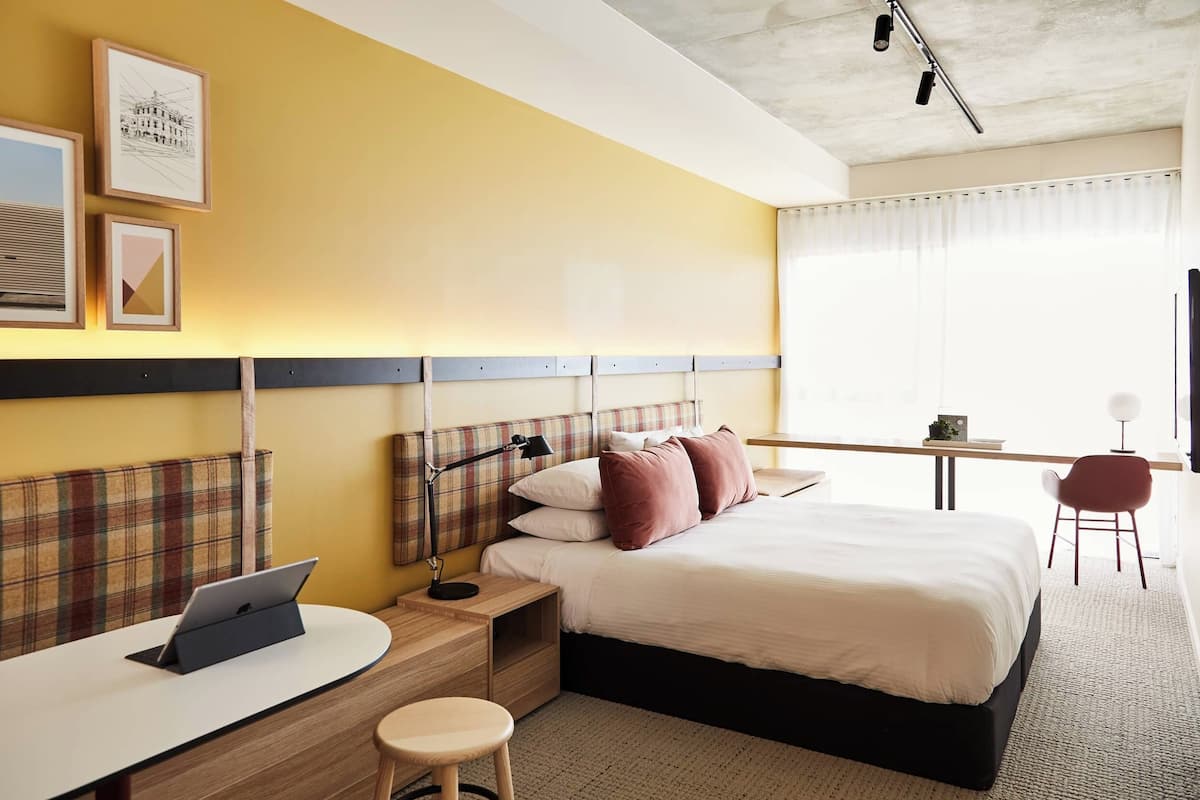 Una habitación de hotel con cama, mesita de noche, lámpara, ordenador portátil y escritorio con silla.