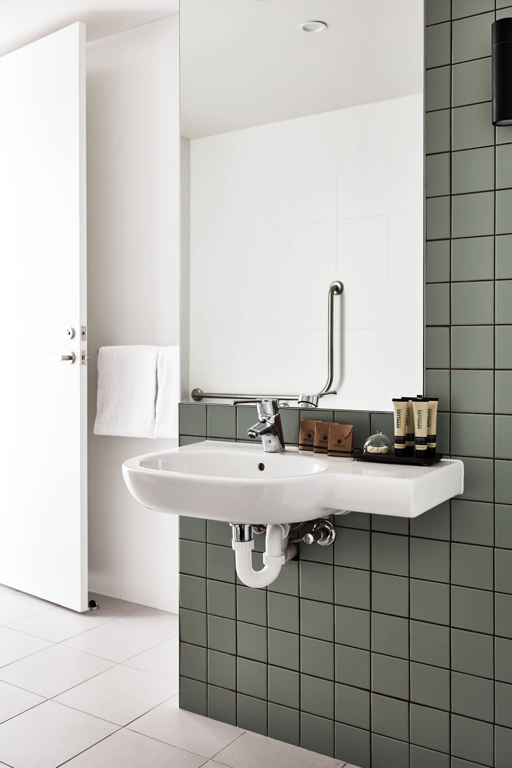 A bathroom with a white sink, a mirror, and green tiles.