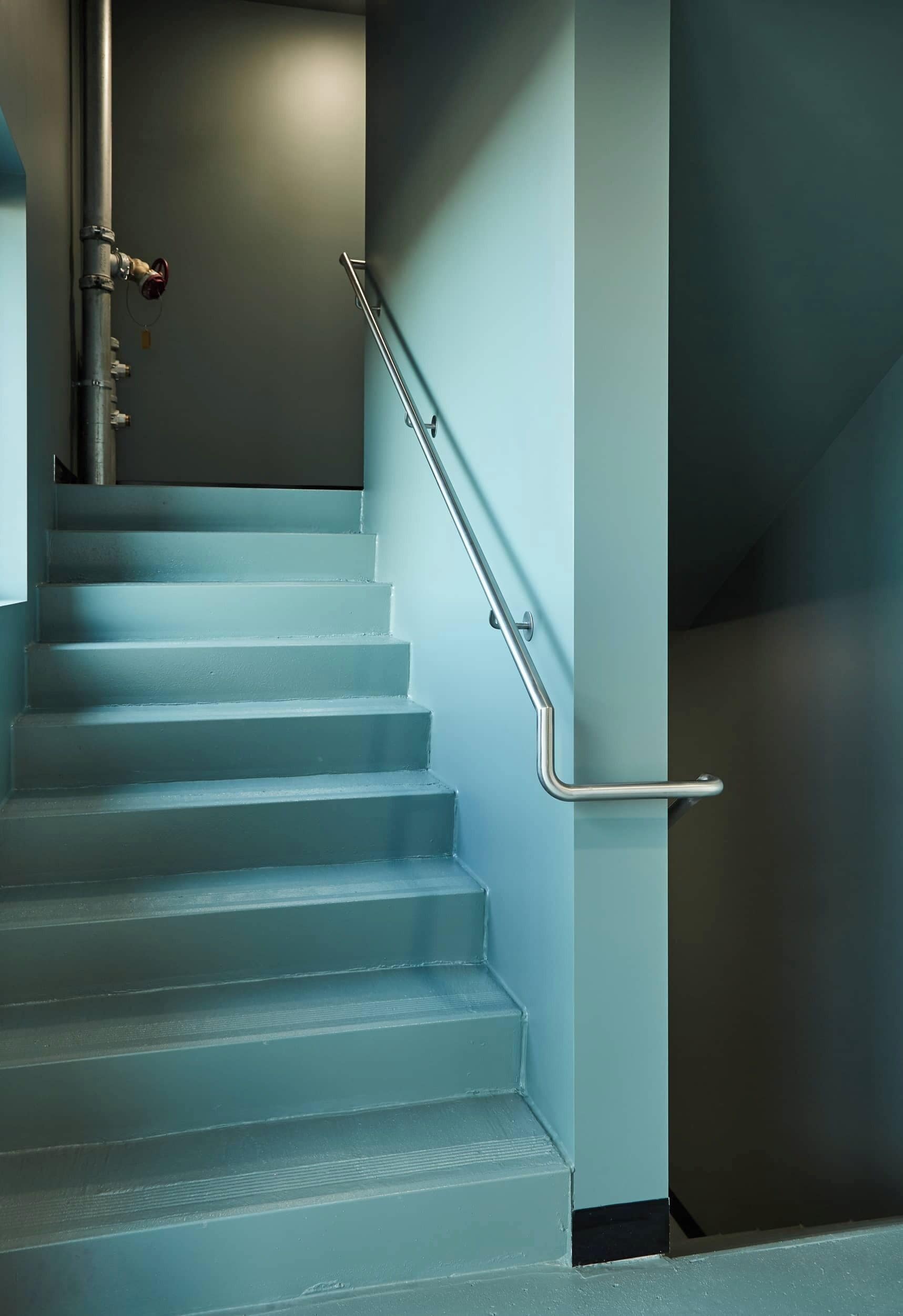 A staircase with a metal handrail and a pipe running along the wall.