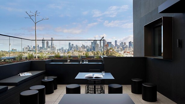 Une terrasse sur le toit offrant une vue panoramique sur la ville, une table avec des chaises et un coin salon avec un livre et un verre.