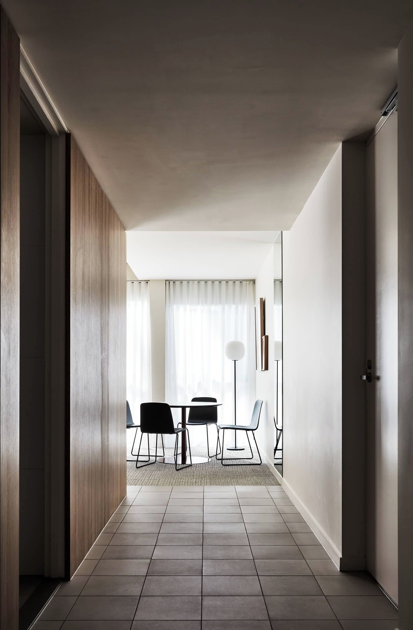 A modern interior with a tiled floor, a dining area with chairs and a table, and a large mirror on the wall.