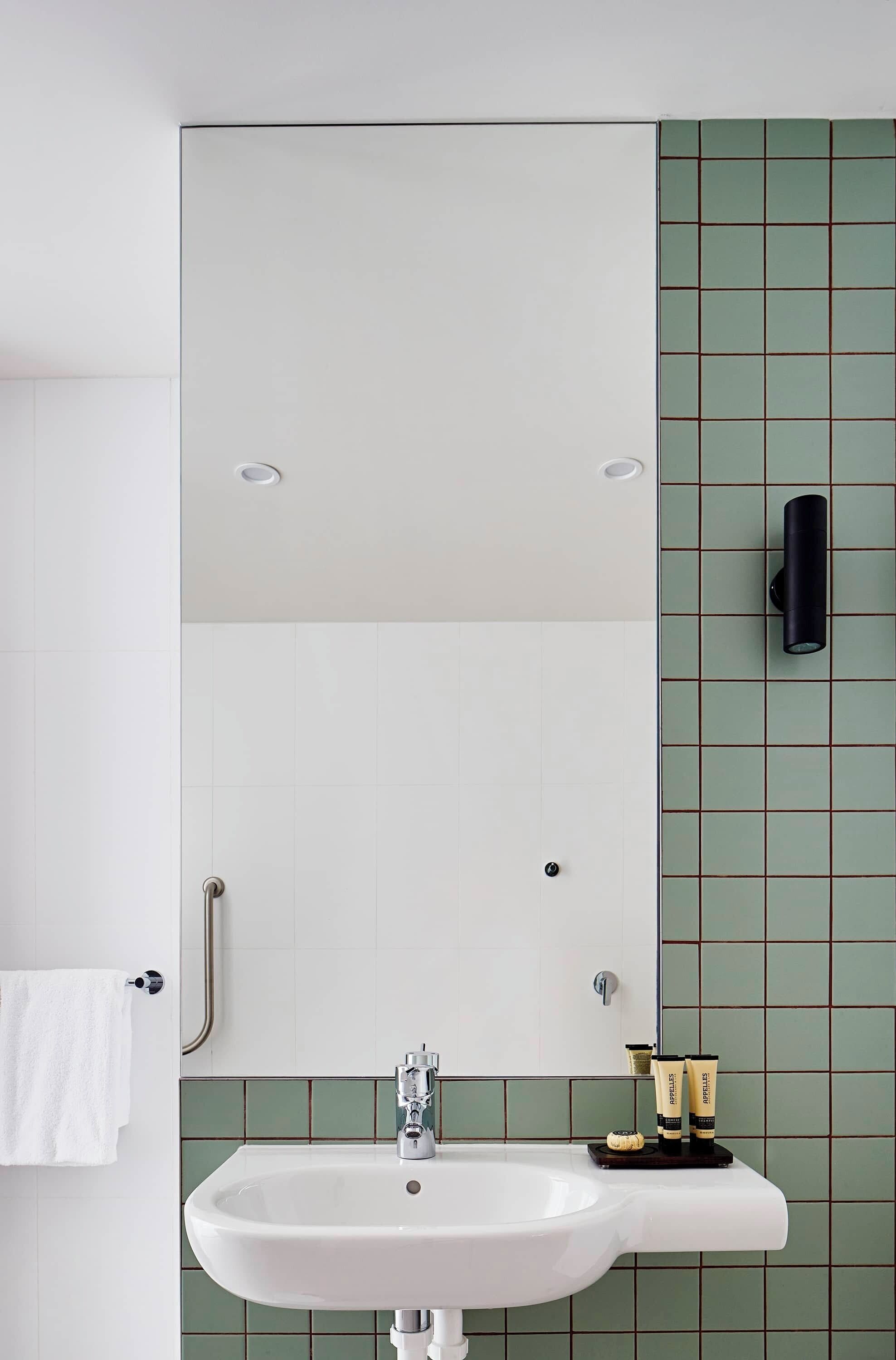A bathroom with a white sink, green tiled walls, a towel rack, and a soap dispenser.