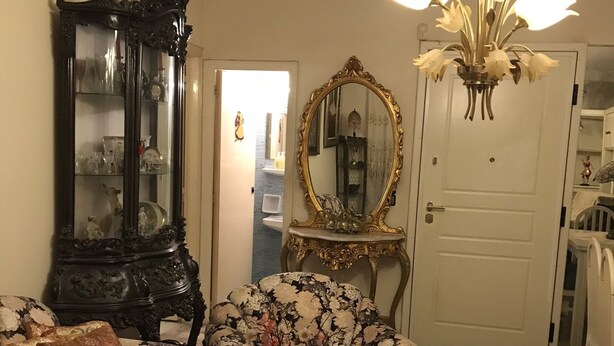 A living room with a floral sofa, a dark wooden cabinet, a glass coffee table, and a chandelier. - Luxury flat, close to city center (Zografou Athens)