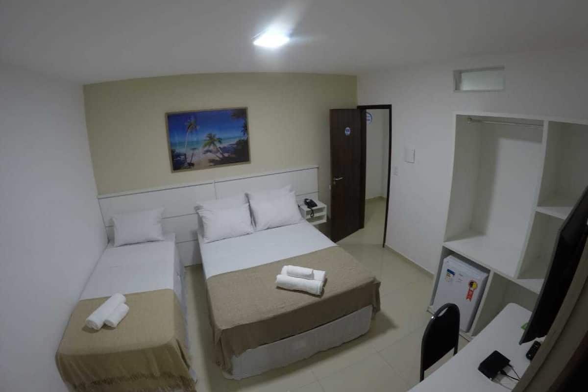 Ein Hotelzimmer mit zwei Betten, einem Schreibtisch, einem Stuhl, einem kleinen Kühlschrank und einem Bild an der Wand.