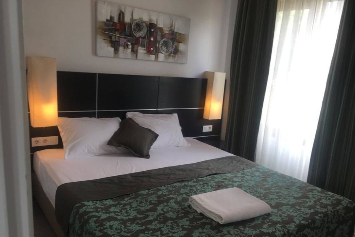 Una cama bien hecha con un edredón estampado, dos lámparas de noche y una obra de arte colgada en la pared sobre la cama.
