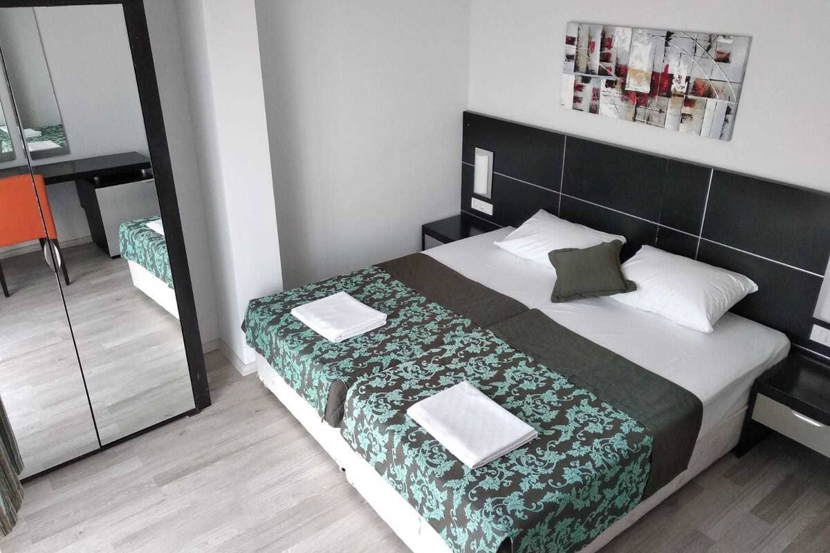 Habitación de hotel ordenada con cama, mesita de noche, una silla y un espejo.