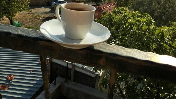 A cup of coffee on a balcony overlooking a town with houses and greenery. - Tepedeki Ev Apart (Gomec)