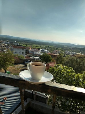 A cup of coffee on a balcony overlooking a town with houses and greenery. - Tepedeki Ev Apart (Gomec)