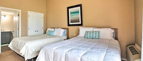 A bedroom with two beds, beige walls, a framed picture, and a ceiling fan.