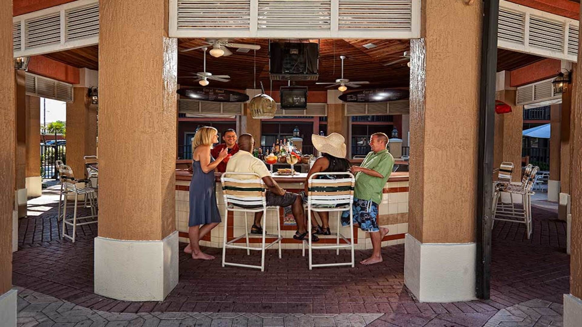 Ein Außenbereich zum Essen mit einer überdachten Terrasse, Tischen, Stühlen und einem Deckenventilator.