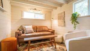A cozy room with a wooden bench, a cushioned sofa, a small round ottoman, and a hanging plant. - Oddfellow Inn & Farm (Helena)
