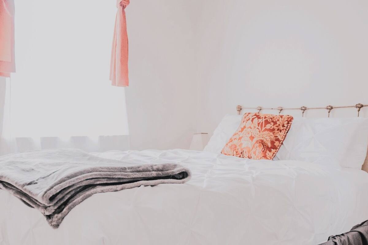Un letto rifatto con cura, con un cuscino a fiori, una coperta e una tenda appesa.