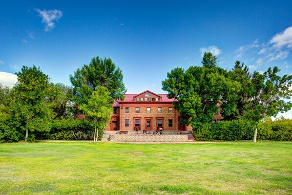 A large red brick building with a symmetrical facade, surrounded by a well-maintained lawn and mature trees.