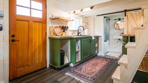 A kitchen with a wooden door, green cabinets, a window, and a rug. - Oddfellow Inn & Farm (Helena)