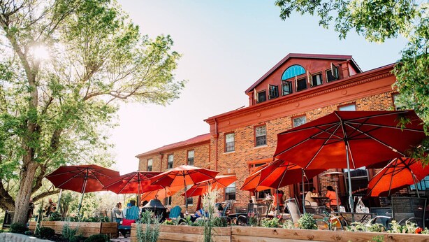 A brick building with outdoor seating and red umbrellas. - Oddfellow Inn & Farm (Helena)