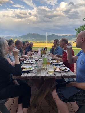 A group of people dining at an outdoor wooden table with a view of mountains in the background.