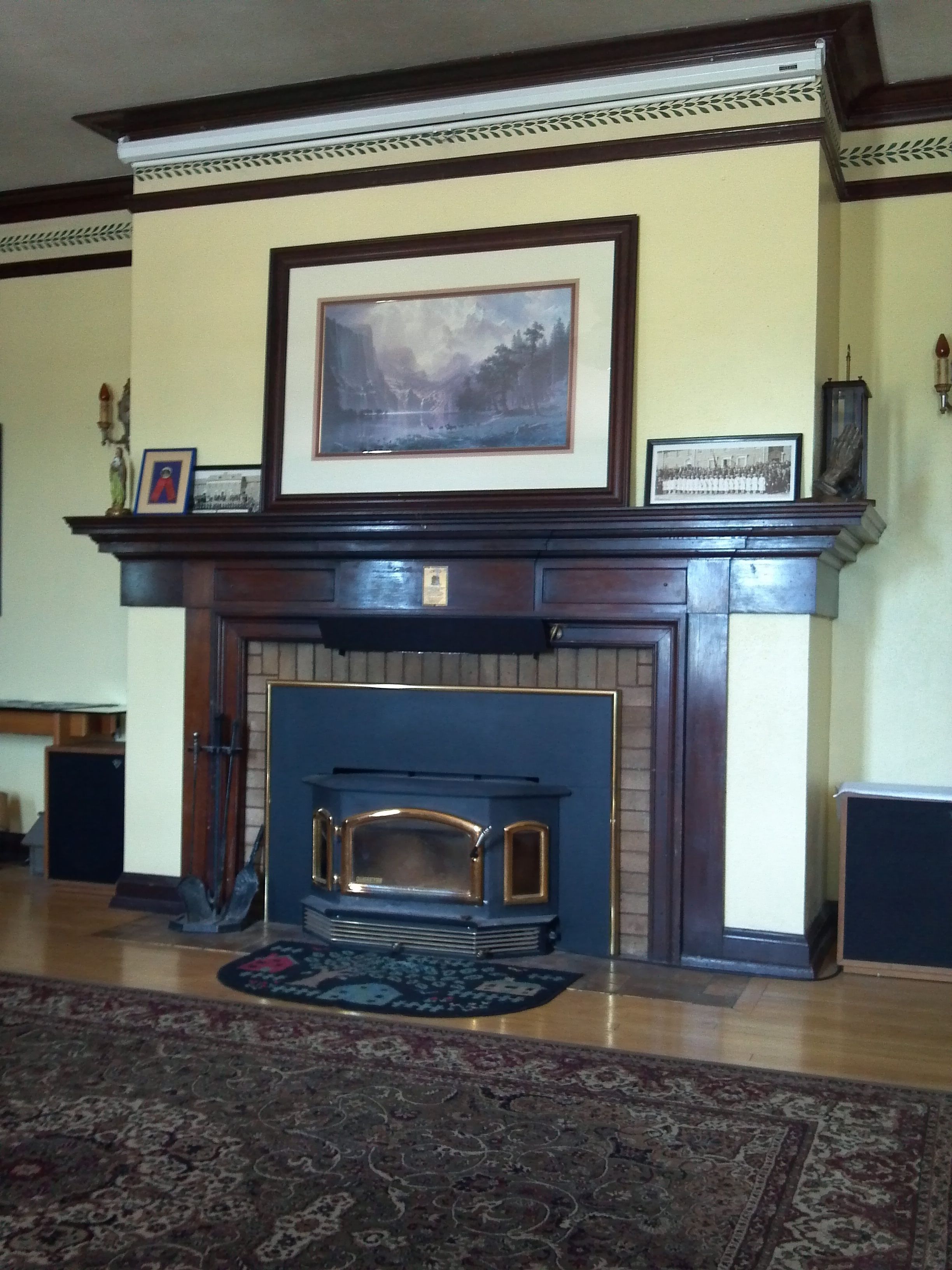 A fireplace with a mantel, framed artwork, and a rug in a room with wooden flooring.