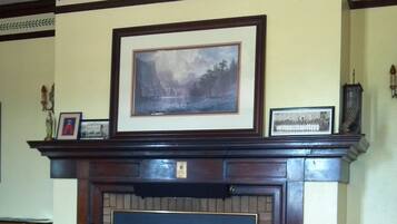 A fireplace with a mantel, framed artwork, and a rug in a room with wooden flooring.