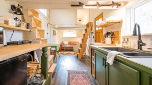 A compact kitchen with wooden shelves, a dining area with a sofa, and a large window providing natural light. - Oddfellow Inn & Farm (Helena)