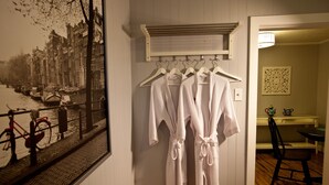 Ein Zimmer mit Holzboden, einer wandmontierten Klimaanlage, einem gerahmten Bild einer Kanalansicht und einem Koffergestell mit weißen Bademänteln.