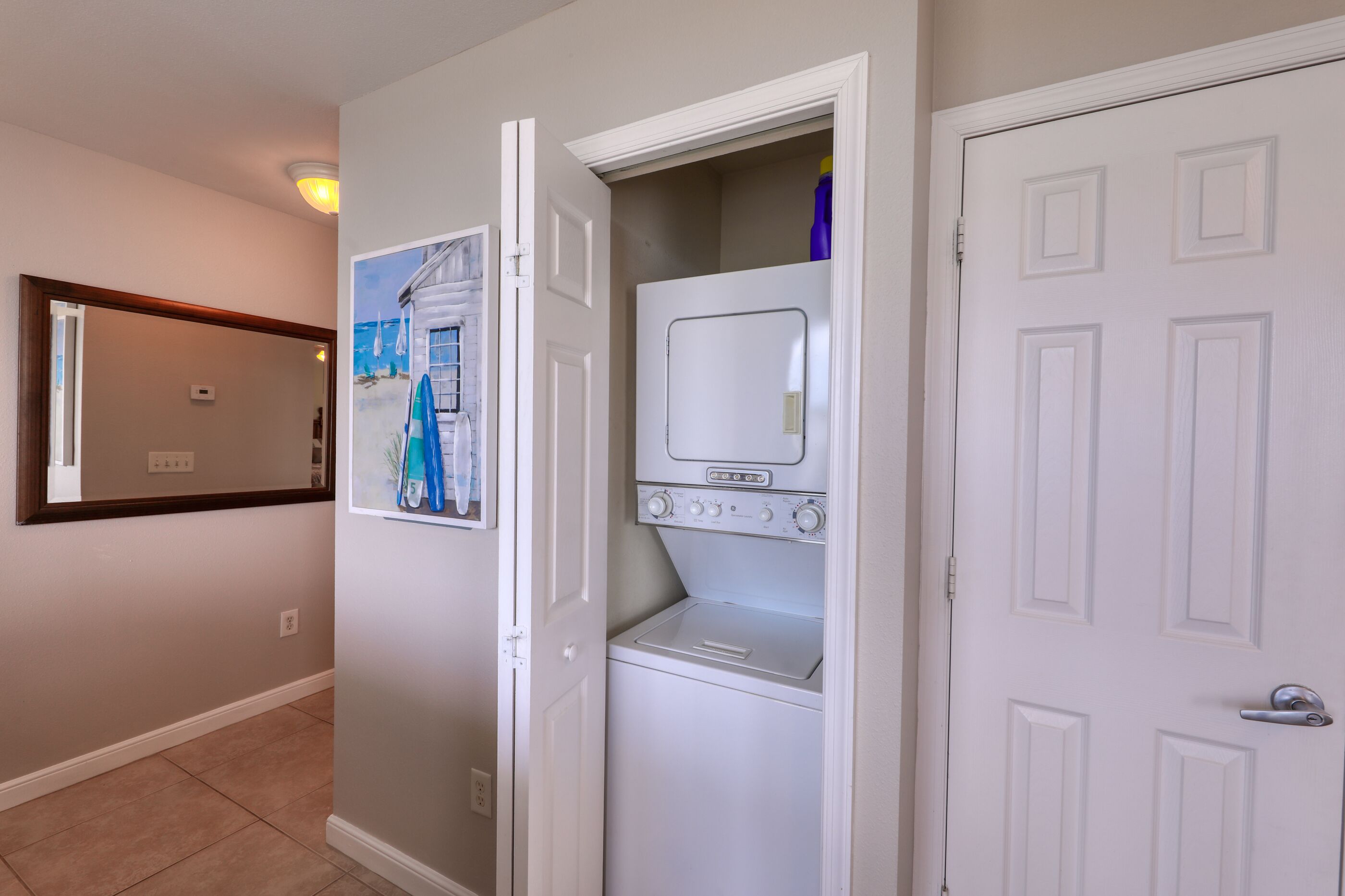 A laundry room with a washing machine and dryer, a door with a mirror, and a wall-mounted light fixture.