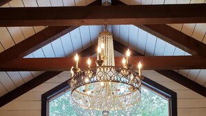 A room with a chandelier, a large window, and a chair with a vase of flowers. - The Bridge House located in an Beautiful RV Resort near Lake Conroe.  (Montgomery)