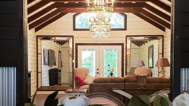A wooden interior with a chandelier, a dining table with a vase of flowers, and a view into a living area with a sofa and a lamp. - The Bridge House located in an Beautiful RV Resort near Lake Conroe.  (Montgomery)