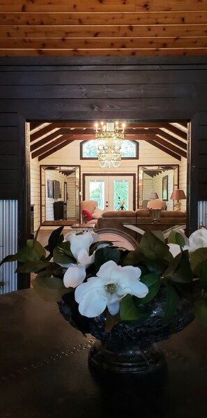 Un intérieur en bois agrémenté d’un lustre, une table à manger ornée d’un vase de fleurs et une vue sur un espace de vie comprenant un canapé et une lampe.