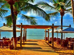 A beachside restaurant with outdoor seating, palm trees, and a view of the ocean. - Bem Bahia Hotel (Porto Seguro)