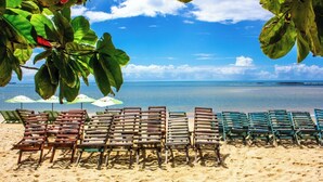 A beach with rows of wooden lounge chairs and umbrellas, a clear blue sky, and calm ocean waters. - Bem Bahia Hotel (Porto Seguro)