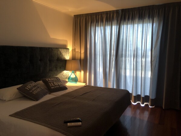 A hotel room with a large bed, a headboard, a bedside lamp, a remote control, and a window with curtains. - Large 6 rooms Luxury Home with Pool and Hot tub (Aflitos)