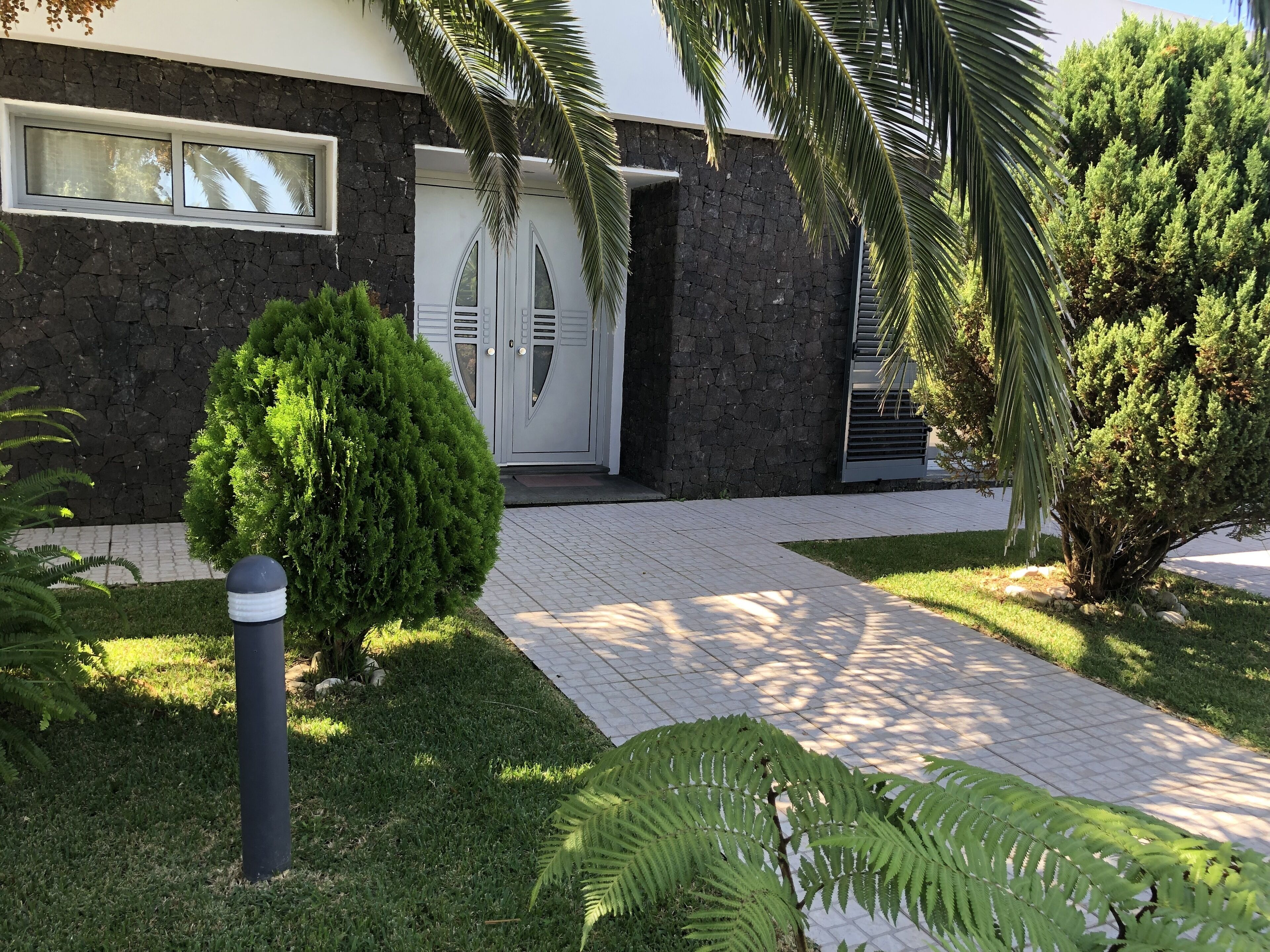 A modern building with a stone facade, a well-maintained lawn, and a pathway leading to a door with a decorative design.