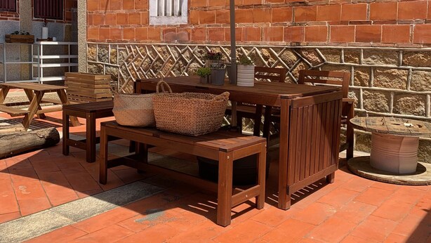 An outdoor patio with a wooden table and chairs, a beige umbrella, and a brick wall. - Yamaharuka B&B (Jinhu)