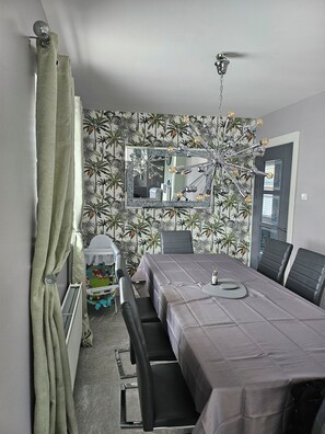 Ein Zimmer mit Esstisch, Stühlen, einem Spiegel, einem Deckenventilator und einem Heizkörper.